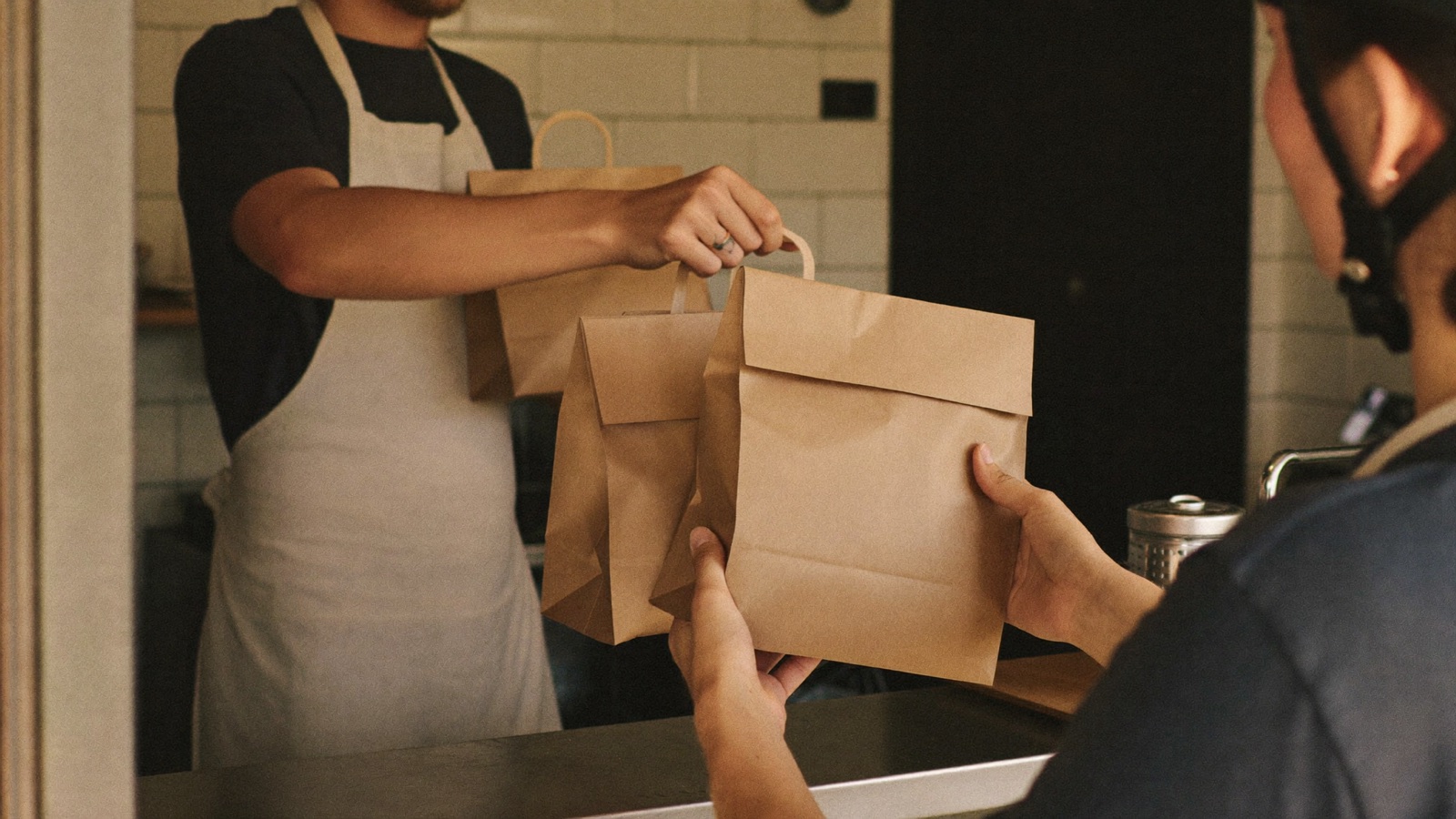 Chef handing takeaway bags to a delivery rider at the counter